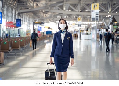 Cabin Crew Or Air Hostess Wearing Face Mask Walking In Airport Terminal To The Airplanel During The COVID Pandemic To Prevent Coronavirus Infection. New Normal Lifestyle In Air Transport Concept.