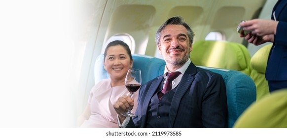 Cabin Crew Or Flight Attendant Serving Red Wine To Businessman In Business Class Passenger Zone After Airplane Taking Off 