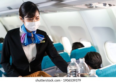 Cabin Crew Pushing Service Cart And Serve To Customer On The Airplane During Flight. New Normal, Flight Attendant And All Passengers Wearing Face Mask To Prevent COVID Infection During Virus Pandemic.