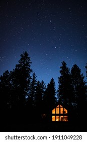 Cabin Illuminated By Soft Orange Light Under A Star-filled Night In The Woods