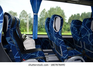 The Cabin Of The Tour Bus Without People. Blue Chairs With High Backs. There's A White Bag On The Seat. There Are Green Silhouettes Of Trees Outside The Windows.