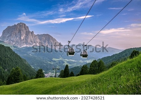Cabins of a ropeway in the Italian Dolomites during sunset with the rocky mountain ranges in the background.