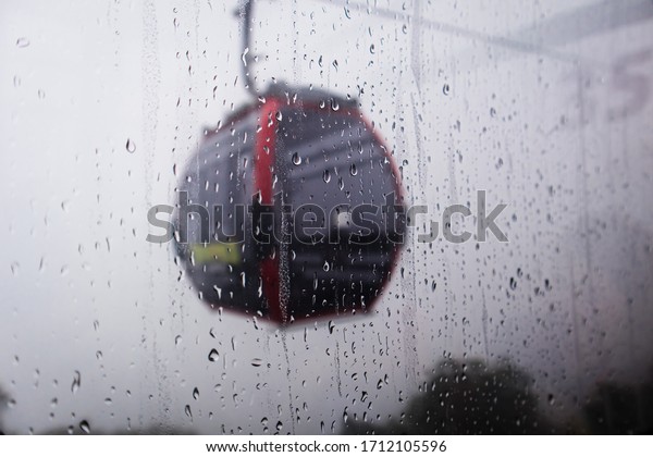 Cable car above green forest in misty clouds\
and water drops falling down on\
window