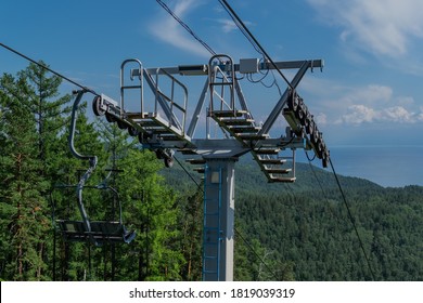 cable car construction with seats among coniferous trees in green forest on hill in mountains, sunny summer blue sky, baikal lake