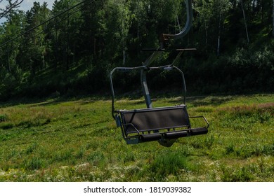 cable car empty seat among trees, grass field in green forest on hill, sunny summer