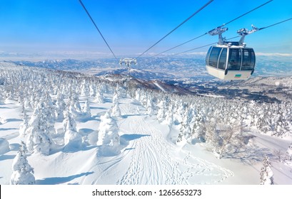 A cable car flying over a piste in Zao hot spring & ski resort with a scenic view of Juhyo forests (ice trees, snow monsters) on the slope under blue clear sky on a sunny winter day in Yamagata, Japan - Powered by Shutterstock