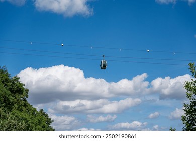 A cable car is flying through the sky above a forest. The sky is mostly clear, with a few clouds scattered throughout. The cable car is suspended high above the trees. The scene is peaceful - Powered by Shutterstock