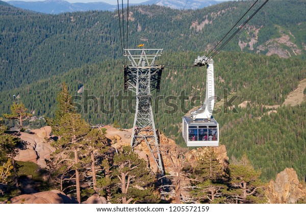A cable car gondola moves\
toward a cable support structure to hold up the cables. The cable\
car holds many people. The cable structure stands on rugged\
mountain peak.