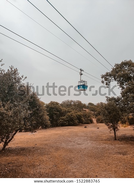 Cable car gondola passing through leafy trees and\
buildings skyline, in a sunny day at the Teleferico Park of Madrid.\
\
View of Madrid from the cable car September 2019. Park near the\
cable car.