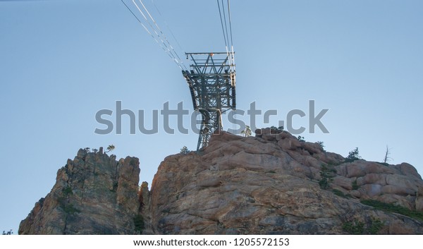 A cable car gondola support structure stands on
the top of the mountain. Cables run through the support system. A
blue sky and mountains are behind the structure. This is a
horizontal image.