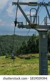 cable car metal construction with empty seats among green trees, grass field in forest on hill, sunny summer blue sky with white clounds, sea on horizon