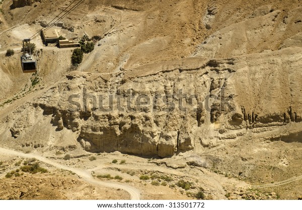 Cable car\
moving over cliffs of Masada fortress in Israel. Ancient sights of\
Middle East deserts for tourists\
attraction