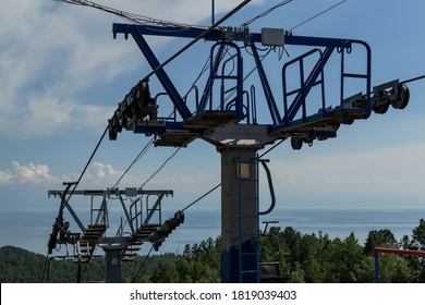 cable car pillars construction among trees in green forest on hill, blue sky with white clounds, sea on horizon