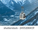 Cable car in ski area of French Alps over the town of Chamonix with beautiful valley, forest, snow and mountains in the background; cable car gondola travelling up cables in Alps, near Mont Blanc
