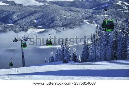 A cable car used for ski lifting above a ski slope. The slopes are located above a valley in a mountainous area with spruce trees. Fog covers the valley. Winter, Carpathia, Romania.