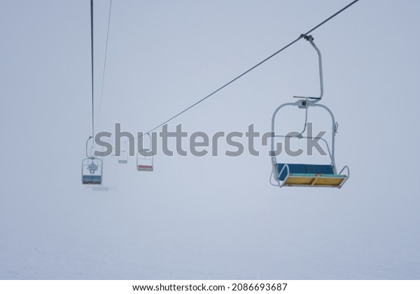 Cable cars hang on cables in a silent ski resort\
against a foggy sky