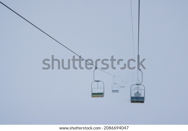 Cable cars hang on cables in a silent ski resort
against a foggy sky