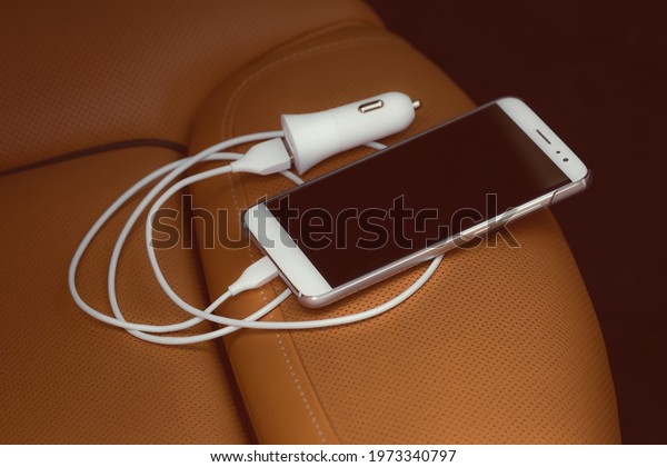 Cable charger for mobile phones with\
smartphone on the leather seat of a luxury\
car