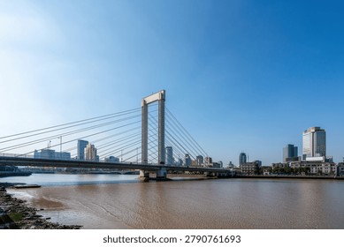 Cable stayed bridge over muddy urban river under clear blue sky