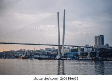 Cable stayed bridge spanning golden horn bay, with bustling port and cityscape of vladivostok in the background, during a vibrant sunset