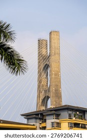 Cable stayed bridge tower rising above residential buildings with palm tree in foreground showcasing modern urban infrastructure and architecture in Guangzhou China