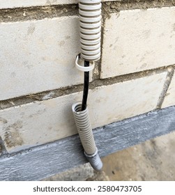 Cable in a torn corrugated pipe on the wall of a building
