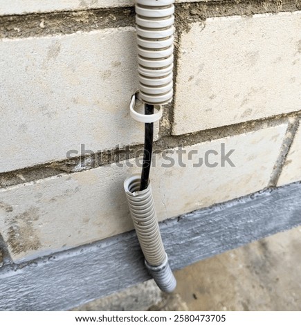 Cable in a torn corrugated pipe on the wall of a building