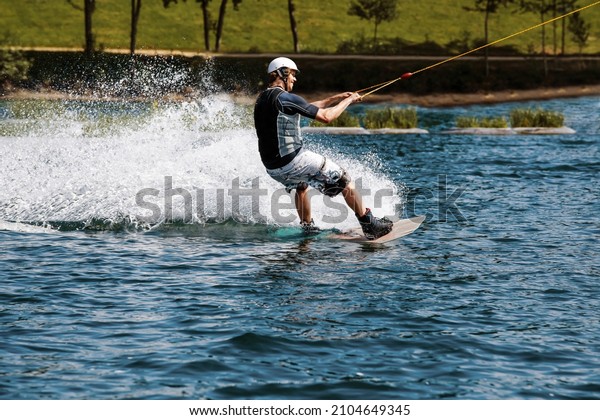 cable wakeboard with a man on it who got pulled\
by rope over lake at a wake\
park