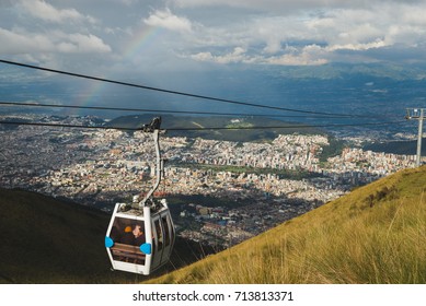 Cable Way Cabin With Rainbow Hanging Above The Houses Of The City Of Quito In Ecuador, South America.  Called Teleférico Or TelefériQo, It Is One Of The Highest Aerial Lifts In The World.