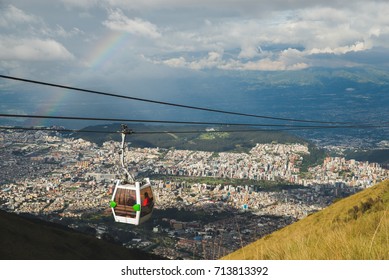 Cable Way Cabin With Rainbow Hanging Above The Houses Of The City Of Quito In Ecuador, South America.  Called Teleférico Or TelefériQo, It Is One Of The Highest Aerial Lifts In The World.