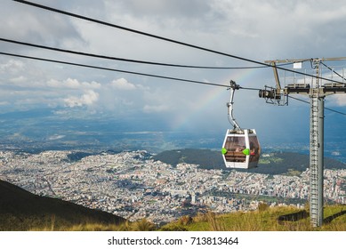 Cable Way Cabin With Rainbow Hanging Above The Houses Of The City Of Quito In Ecuador, South America.  Called Teleférico Or TelefériQo, It Is One Of The Highest Aerial Lifts In The World.