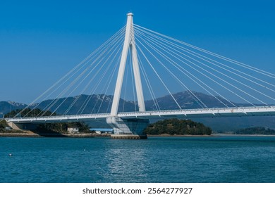A cable-stayed bridge spanning across a ocean inlet with mountains in the background under a clear blue sky, located in Wando, South Korea