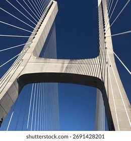 Cable-stayed bridge under blue sky. 
Low-angle view of a modern suspension bridge against a deep blue sky. The strong lines create a sense of scale and engineering elegance.