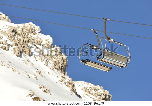 Cableway in alpen mountains. Chair lift with\
rock, snow and blue sky in the\
background.