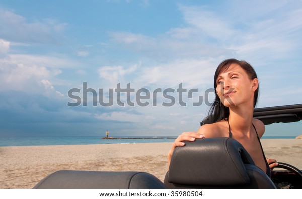 Cabriolet woman parking on the beach with\
ocean sea and coastline in\
background