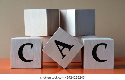 CAC - acronym on large wooden cubes on light brown background. Business concept