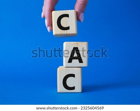 CAC - Customer Acquisition Cost symbol. Wooden cubes with word CAC. Beautiful blue background. Businessman hand. Business and Customer Acquisition Cost concept. Copy space.