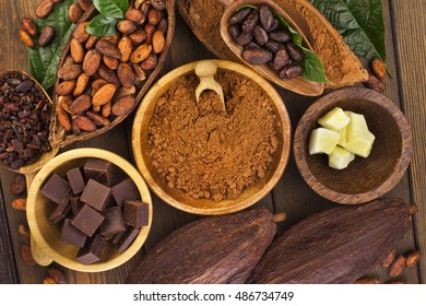 Cacao beans and powder, cacao butter and cacao nibs with chocolate on a wooden background