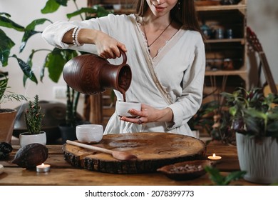 Cacao Ceremony In Atmospheric Space With Green Plants And Candles. Woman Making Ritual Healthy Drink From Cocoa Beans. Person Pouring Fresh Made Hot Chocolate Drink Into Jar 