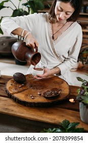 Cacao Ceremony In Atmospheric Space With Green Plants And Candles. Woman Making Ritual Healthy Drink From Cocoa Beans. Person Pouring Fresh Made Hot Chocolate Drink Into Jar 