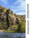 Cache la Poudre canyon as it approaches Fort Collins, CO.  Huge rock bluff, blue sky and trees.  Rocky background.  Reflective water. Scenic area with blue sky, Tall mountain, green bushes and trees.