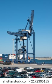 Cadiz, Spain. May 22nd 2022. A Shipping Container Crane Stands At A Dock With A Busy Car Park In The Foreground. Blue Sky And A Blue Crane Dominate The Scene.