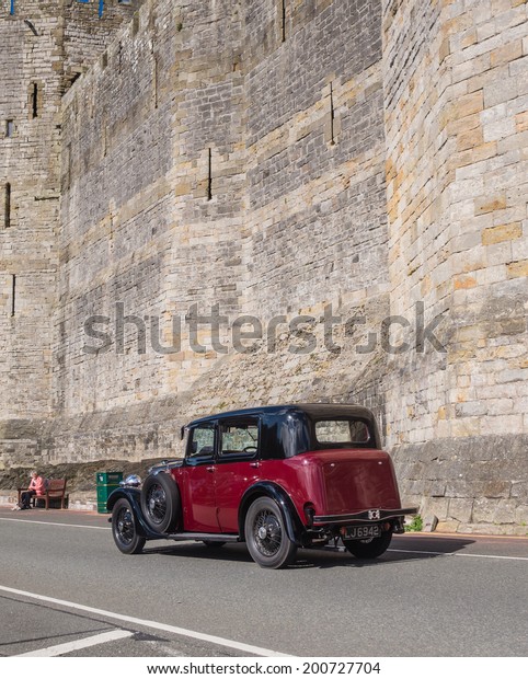 CAERNARFON, WALES\
- 29 SEPTEMBER 2013: Vintage classic car taking part in the Walled\
Towns Trail Car Run 2013 passes the walls of Caernarfon Castle en\
route to its next\
destination