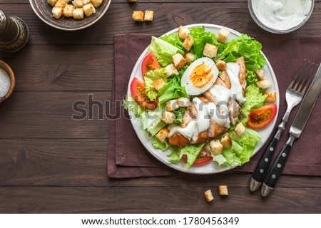 Caesar salad with chicken breast on dark wooden background, top view, copy space. Fresh chicken salad for healthy lunch.