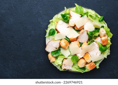 Caesar salad with chicken, iceberg salad, croutons, parmesan cheese with caesar dressing. Traditional recipe. Black table background, top view