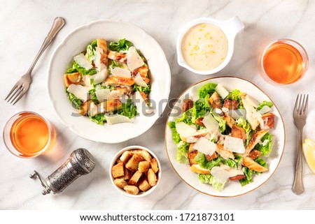 Caesar salad with the classic sauce and wine, shot from the top on a white marble background