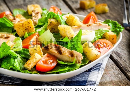 Caesar salad with croutons, quail eggs, cherry tomatoes and grilled chicken on wooden table