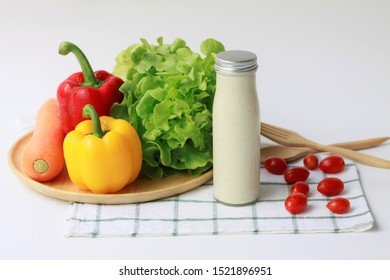 Caesar Salad Dressing In Glass Bottle With Ingredient Of Vegetable Salad, Green Oak Lettuce, Bell Peppers, Carrot And Tomatoes On Green And White Checkered Napkin On White Background