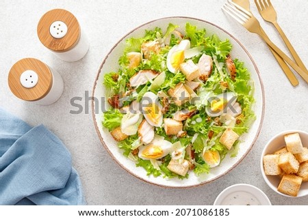 Caesar salad with grilled chicken breast, hard-boiled egg, croutons, parmesan cheese, green salad lettuce and dressing. Top view.