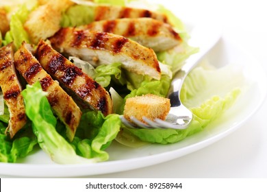 Caesar Salad mit gegrilltem Huhn auf weißem Teller.